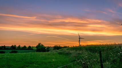 Fototapeta na wymiar Wind mill at dramatic sunset with fields of fresh grass