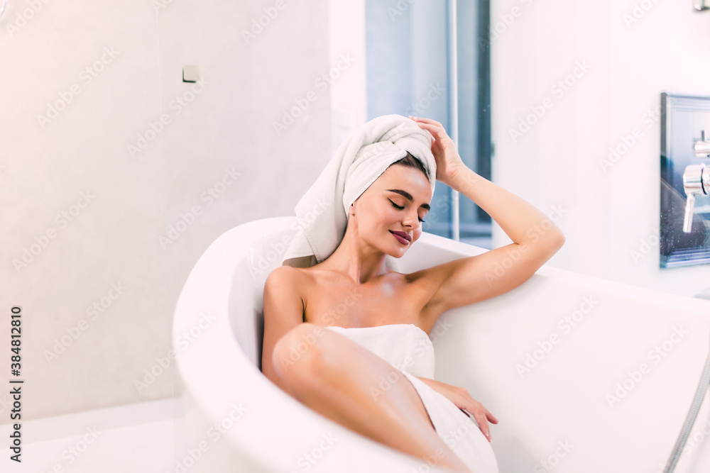 Wall mural young pretty woman wearing a bathrobe sitting on the bathtub