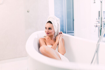 Beautiful young woman in bathrobe lying in bathtub. Self care concept.