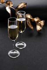 Two glasses of champagne over black background and golden Christmas decoration. Holiday decorations on dark table.