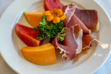 Arrangement of Delicatessen Cold Cuts with charcuterie, melon and watermelon decorated with orange flower and parsley. Soft focus background