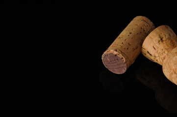 Two old wine corks on a black background with reflection