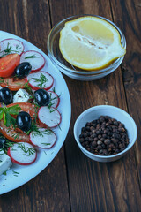 a plate of salad with red tomato, black pepper and cheese on a wooden table