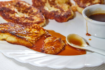 Pancakes on white plate and sweet liquid honey or caramel with a small spoon and with background. Delicious fried flour food. Unhealthy and harmful, but very tasty food.