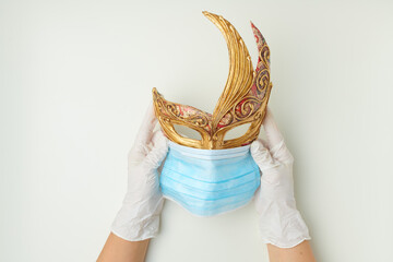 hands in rubber gloves holding venetian mask in medical mask