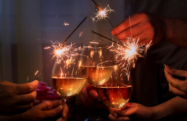 glasses with sparkling wine and sparkler is held by a company of people