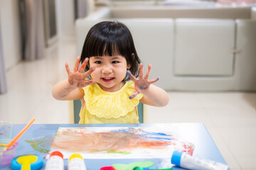 happy Toddler painting water color with her hand. smiley baby girl with painted hand. - 384821247