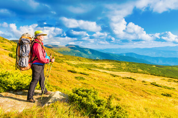 Naklejka premium Happy traveling woman with backpack looking at mountain landscape