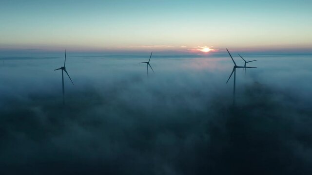 Wind turbine at sunrise in heavy fog. Wind farm generating green energy