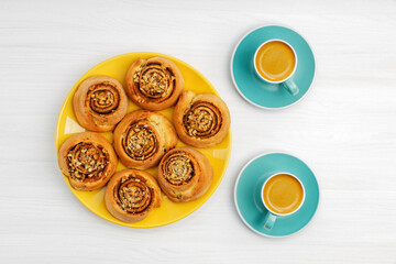 Obraz na płótnie Canvas Homemade cinnamon rolls from yeast dough and two cups of coffee espresso on white wooden table. Top view.