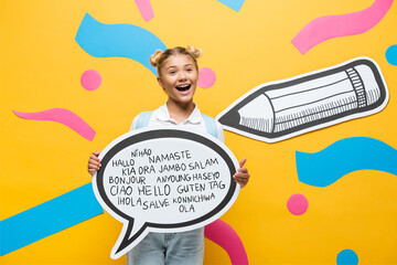 excited schoolchild holding speech bubble with greeting lettering near multicolored paper elements and pencil on yellow © LIGHTFIELD STUDIOS
