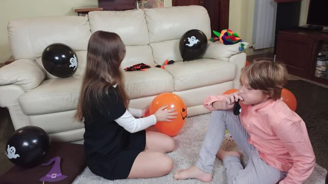 Girl and boy, sister and brother are Inflating Halloween baloons, having fun and playing. Children get ready for celebrate Halloween at home, decorate home