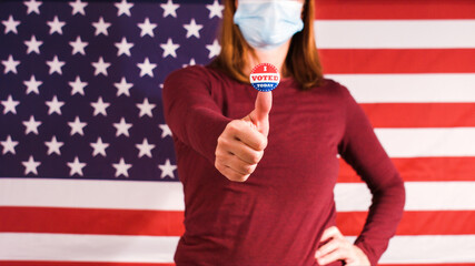 Woman with I voted today sticker on thumbs up finger and face mask at 2020 american elections.