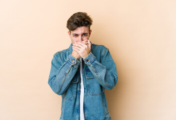 Young caucasian man isolated on beige background covering mouth with hands looking worried.