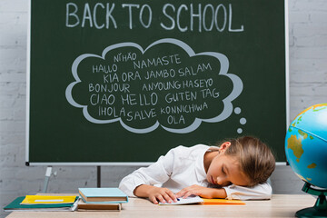 exhausted schoolgirl sleeping at desk near globe and chalkboard with back to school and greeting lettering © LIGHTFIELD STUDIOS
