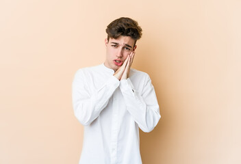 Young caucasian man isolated on beige background yawning showing a tired gesture covering mouth with hand.