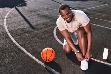 Fototapeta premium Joyful man tying his shoelaces on a basketball court