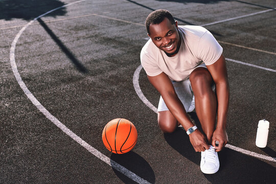 Joyful man tying his shoelaces on a basketball court