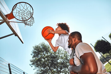 Afro-American kid playing basketball with his father