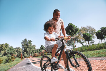 Focused child riding bicycle accompanied by his father