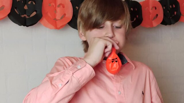 A blond boy enjoying himself waving the orange pumpkins balloon with the face of Jack 'O Lantern, Inflating balloon, Halloween at home with decorations