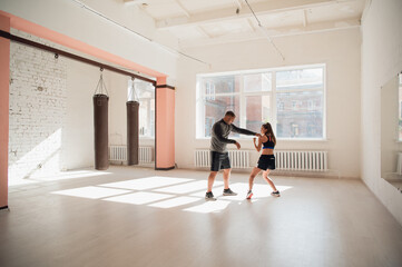 In the boxing hall, an experienced trainer teaches a young girl the correct stance