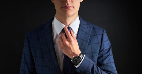 cropped business man straighten a tie isolated over black background. young guy in formal suit...