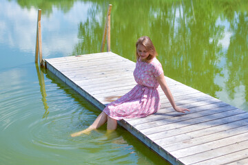 woman on the lake on the pier sits resting in the summer.