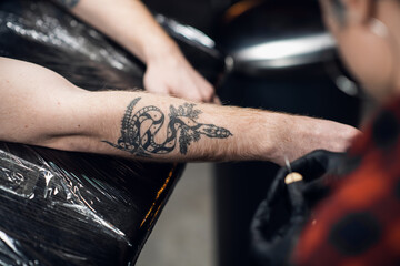 A tattoo artist with short hair and piercings is preparing to get a tattoo on a man's arm in a tattoo parlor.