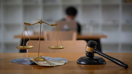 Scales of justice placed on money and lawyer hammer on the table, the background is blurred