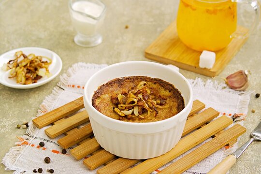 Kugelis, baked potato pudding made from grated raw potatoes in a white portioned baking dish on a concrete gray background.