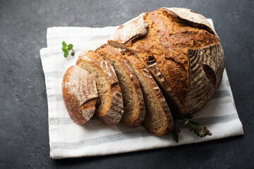 A loaf of fresh dark round buckwheat bread from a private bakery on a dark background on a vintage wooden cutting board. Top view,