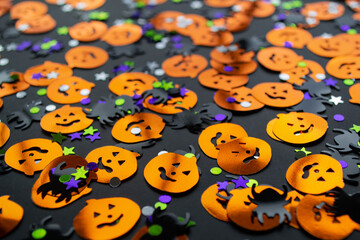 Halloween background: shiny confetti in the shape of orange pumpkins, black spiders and colorful stars green, purple color
