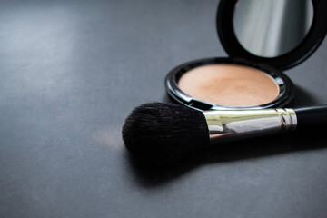 Close-up of a black makeup brush with flesh-colored powder at the end. On the background of an open...