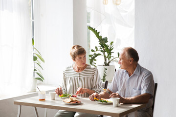 Fototapeta na wymiar Portrait of relaxed fun senior couple together and eating breakfast in their kitchen at home 
