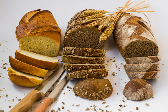 Various of creal breads sliced on white surface with a bunch of wheat ears,cereal grains and knife.