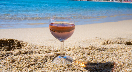 Glass of local rose wine on white sandy beach and blue Mediterranean sea on background, near Le Lavandou, Provence, France