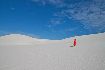 Fotobehang girl in a red dress against a blue sky on white sand © Jolil