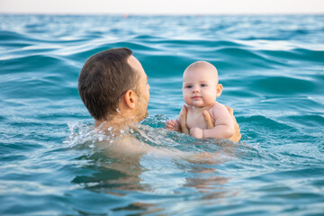 Father with her daughter little baby girl swimming and relaxing in the sea at sunset time