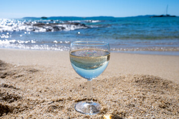 Glass of local dry white wine on white sandy beach and blue Mediterranean sea on background, near Le Lavandou, Provence, France