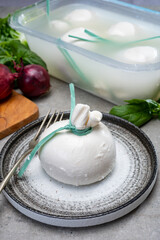 Eating of fresh handmade soft Italian cheese from Puglia, white balls of burrata or burratina cheese made from mozzarella and cream filling in container with water
