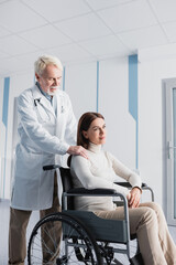 Senior doctor touching shoulder of disabled patient in wheelchair in client