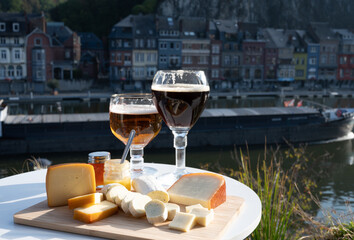 Glass of Belgian abbey beer and tasting of cheeses made with trappist beer and fine herbs with view on Maas river in Dinant, Wallonia, Belgium
