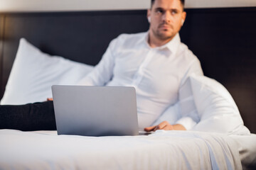 A close up picture of a young man with his laptop in bed.