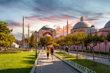 Fototapeta na wymiar Tourists walk through the Hippocrome towards the ancient mosque, church and museum of Hagia Sophia in Sultanahmet Square at sunset, Istanbul Turkey