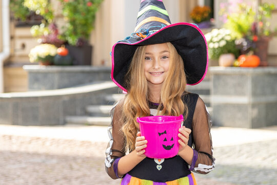 Smiling little girl on Halloween in a witch costume asking for candy.