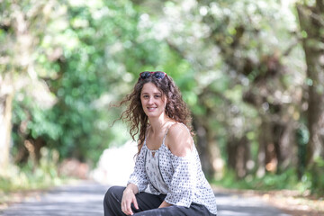 Obraz premium portrait of a woman posing on a lonely road among trees, posing on her knees. He wears a white shirt and black pants