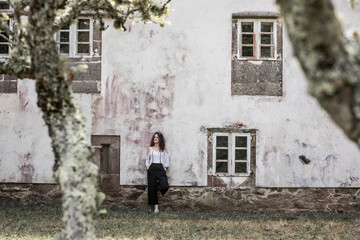 Fototapeta na wymiar Woman leaning on the facade of an old house with white walls and classic windows 
