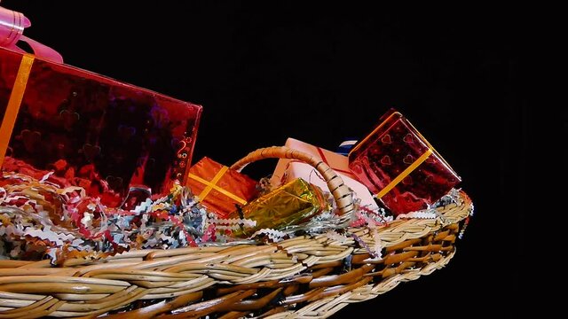 A basket with gifts packed in a colored, shiny wrapper. The basket on a dark background turns in different directions.