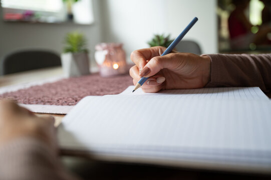 Woman writing in blank notebook on wooden desk